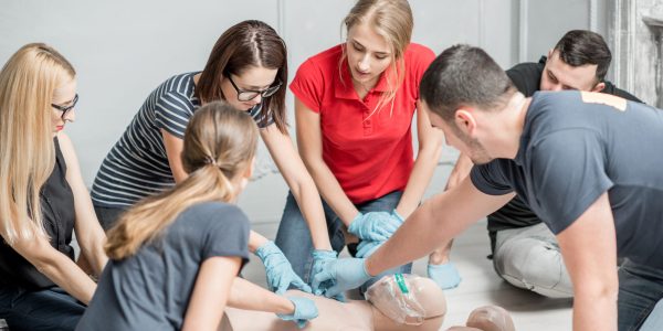 Group of people learning how to make first aid heart compressions with dummies during the training indoors