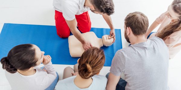 instructor performing cpr on dummy during first aid training with group of people