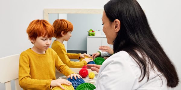 Occupational therapist using sensory integration therapy to improve sensory processing for male child patient. Doctor using hedgehog half balls to develop the boy's fine motor skills