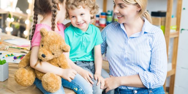 Warm toned portrait of happy young mother with two cute little kids smiling and hugging teddy bear toy