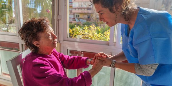 Young nurse comforting elderly woman by holding her hands, providing home care and support