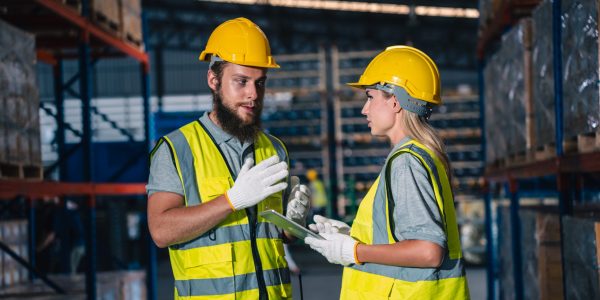 Engineer wearing safety vest controlling industrial machine working, talking with assistant worker checking first for labour with laptop computer, Officer setting a technology system in factory.