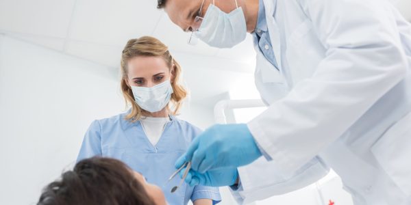 Male dentist and his female assistant checking patient in modern dental clinic
